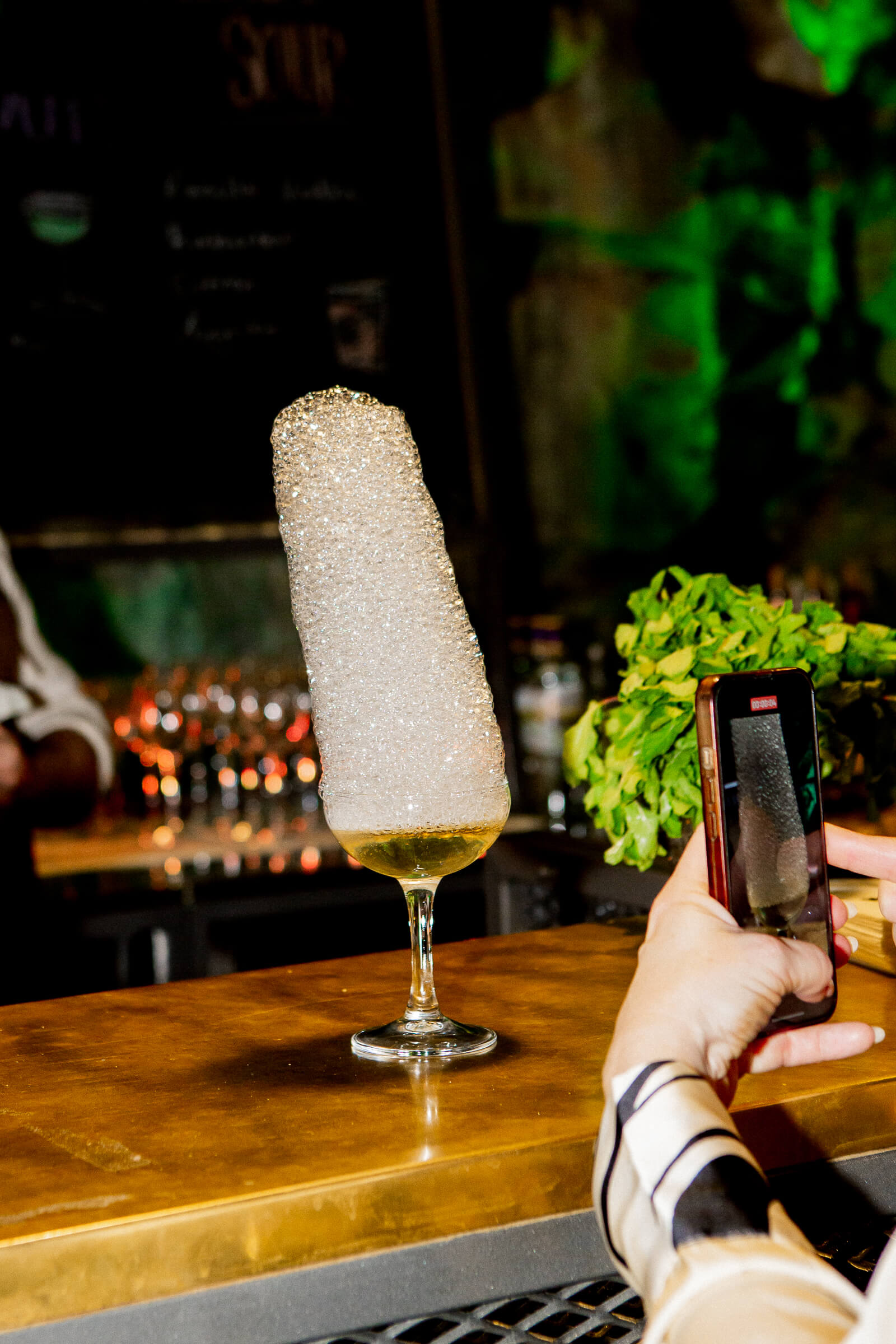 Cocktail med hög skumtopp i ett stjälkglas på en bardisk